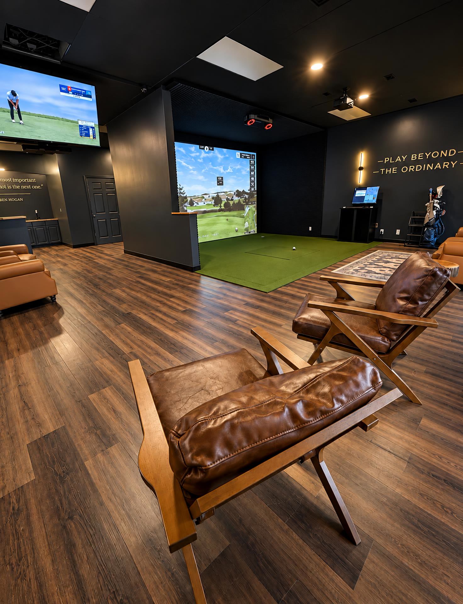 Inside Black Tee Golf Club — leather chairs facing a simulator bay, Play Beyond The Ordinary lettering on the back wall and golf on the TV